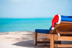 espreguiçadeiras com chapéu de Papai Noel na bela praia tropical com areia branca e água azul-turquesa. férias de natal perfeitas foto