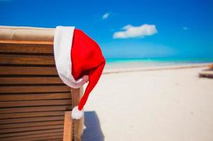 chapéu de papai noel vermelho na cadeira longue na praia tropical do caribe foto