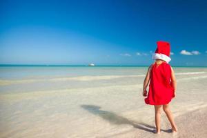 menina adorável com chapéu de Papai Noel vermelho na praia tropical foto