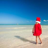 menina adorável com chapéu de Papai Noel vermelho na praia tropical foto