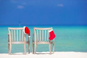 meia vermelha de natal e chapéu de papai noel na cadeira na praia tropical branca foto