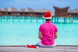 jovem de chapéu de Papai Noel durante as férias de praia no cais de madeira foto