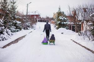 jovem pai rola suas filhas bonitinhas em um trenó na neve ao ar livre foto