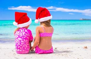 meninas adoráveis em chapéus de Papai Noel durante as férias na praia foto