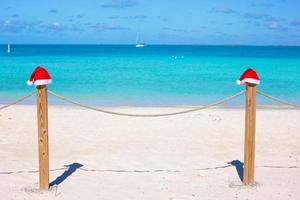 dois gorros de papai noel em cima do muro na praia tropical branca foto