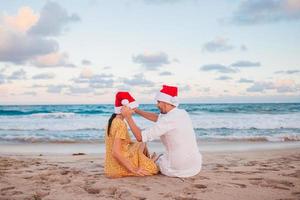 casal feliz de natal em chapéus de papai noel nas férias na praia foto