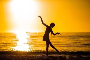 silhueta da linda garota dançando na praia ao pôr do sol foto