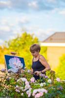 mulher feliz pintando um quadro em um cavalete em um dia quente foto