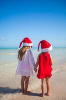 vista traseira de meninas bonitas em chapéus de natal na praia exótica foto