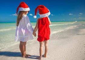 vista traseira de meninas bonitas em chapéus de natal na praia exótica foto