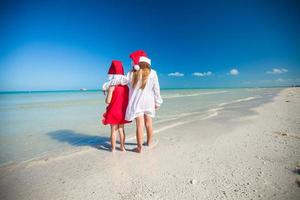 vista traseira de meninas bonitas em chapéus de natal na praia exótica foto