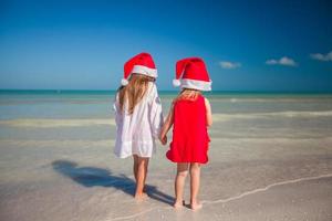 vista traseira de meninas bonitas em chapéus de natal na praia exótica foto