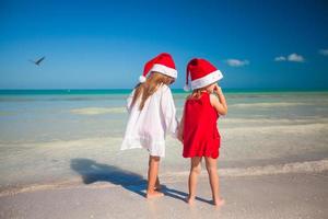 vista traseira de meninas bonitas em chapéus de natal na praia exótica foto