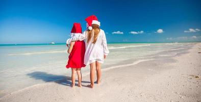 vista traseira de meninas bonitas em chapéus de natal na praia exótica foto