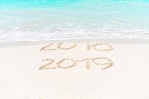 2018 e 2019 escritos à mão na praia com ondas suaves do mar no fundo foto