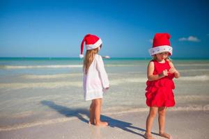 vista traseira de meninas bonitas em chapéus de natal na praia exótica foto