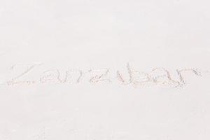 palavra manuscrita na praia de areia com onda do mar suave no fundo foto