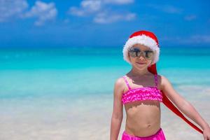 menina adorável com chapéu de Papai Noel vermelho na praia tropical foto