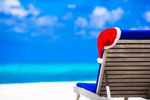 salão de espreguiçadeira com chapéu de papai noel vermelho na praia branca tropical e água azul-turquesa foto