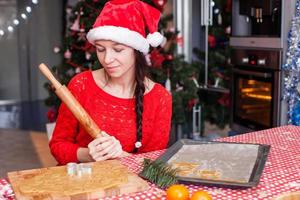 jovem de chapéu de natal assando pão de gengibre em casa foto