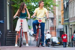 jovem casal caucasiano feliz em bicicletas em ruas antigas de Amsterdã foto