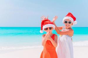 meninas adoráveis em chapéus de papai noel durante as férias de natal na praia se divertindo juntos foto