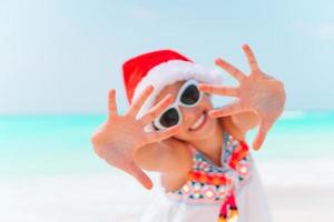 adorável menina com chapéu de Papai Noel em praia tropical foto