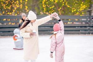 menina adorável com sua mãe patinando na pista de gelo foto