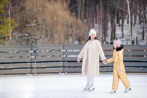 menina adorável com sua mãe patinando na pista de gelo foto