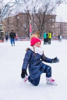 menina adorável sentada no gelo com patins após a queda foto