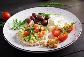 torradas saudáveis de abacate no café da manhã ou almoço, abacate guacamole, azeitonas kalamata, tomate, castanha de caju e queijo feta. sanduíches vegetarianos foto