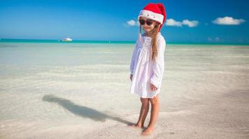 menina adorável com chapéu de Papai Noel vermelho na praia tropical foto