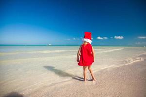 menina adorável com chapéu de Papai Noel vermelho na praia tropical foto