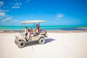 meninas e sua mãe dirigindo carrinho de golfe na praia tropical foto