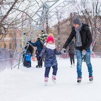 menina adorável e pai feliz na pista de patinação ao ar livre foto