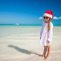 menina adorável com chapéu de Papai Noel vermelho na praia tropical foto