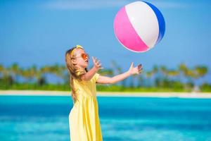 adorável menina brincando na praia com bola ao ar livre foto