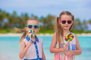 duas meninas com pirulitos saborosos brilhantes na praia branca foto