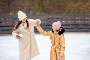 menina adorável com sua mãe patinando na pista de gelo foto