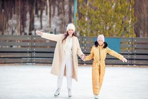 menina adorável com sua mãe patinando na pista de gelo foto