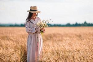 vista traseira da menina no campo de trigo. linda mulher de vestido em um chapéu de palha foto