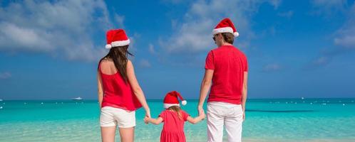 família feliz em chapéus de natal se divertindo na praia branca foto