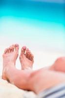 pés femininos na praia de areia branca em águas rasas foto