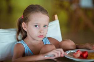 adorável menina tomando café da manhã no café ao ar livre foto