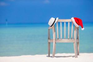 cadeira de praia com Papai Noel vermelho e fundo de chapéu de palha lindo mar turquesa foto