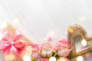 caixa de presente, rosas cor de rosa, coração de madeira em pano de fundo branco de madeira com espaço de cópia de cartão festivo de luzes de bokeh foto