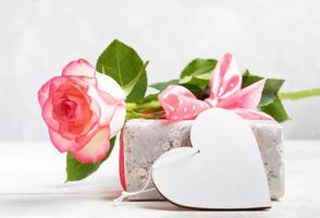 mock up festivo com caixa de presente embrulhada em papel floral, rosa suave, coração de madeira branco vazio. foto