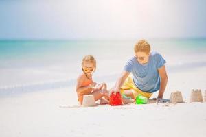 pai e filhos fazendo castelo de areia na praia tropical. família brincando com brinquedos de praia foto