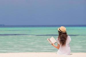 retrato de uma jovem mulher relaxando na praia, lendo um livro foto