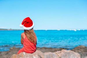 adorável menina com chapéu de Papai Noel em praia tropical foto